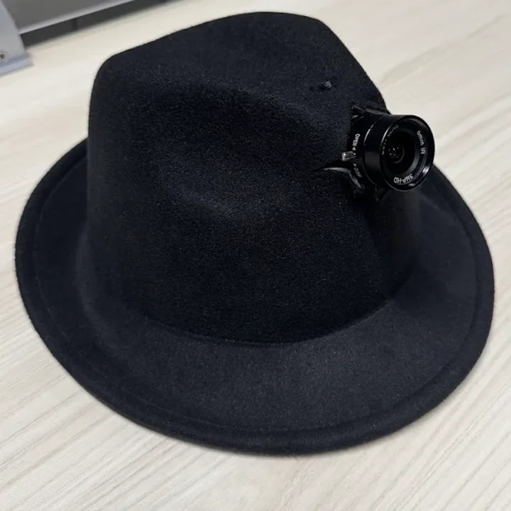The hat on the desk from its front right: the lens turned toward the camera, its markings readable round the glass.