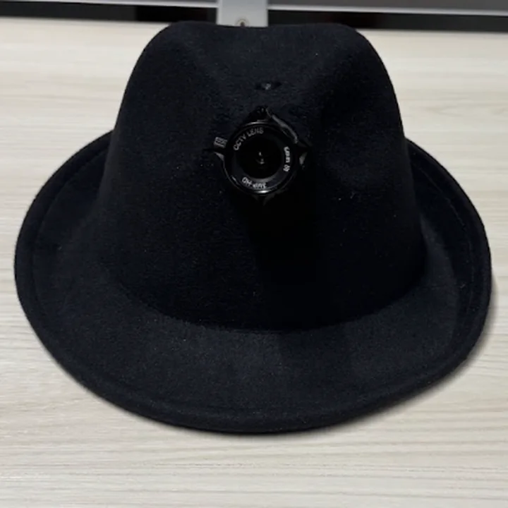 The hat on the desk, head on: the lens in the middle of the crown, held in a cut in the felt.