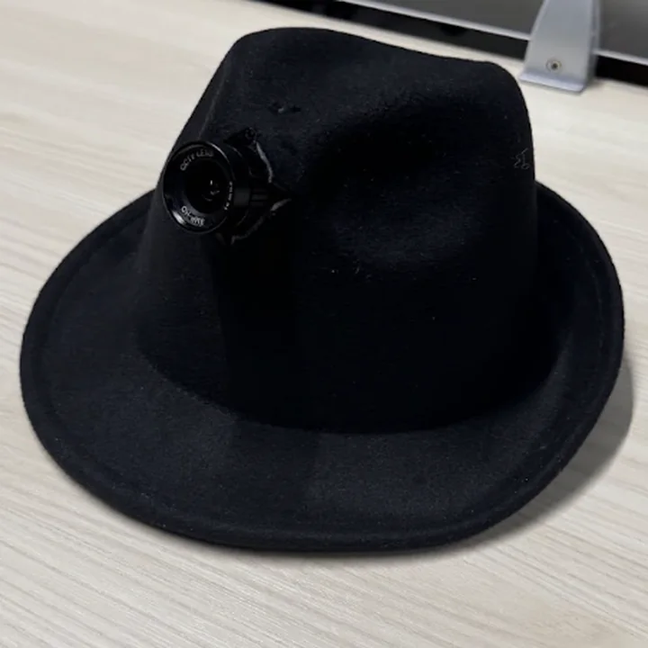 The hat on the desk from its front left: the lens on the left of the crown, angled toward the camera.