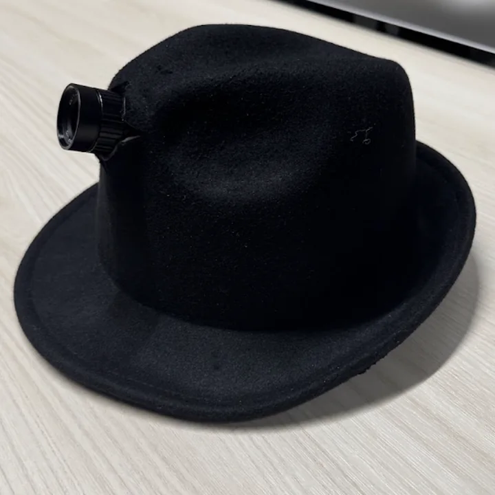 The hat on the desk from its left: the lens barrel pointing left, clear of the crown.