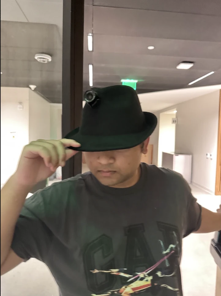 A second crew member wears the hat, the camera lens showing in its crown.