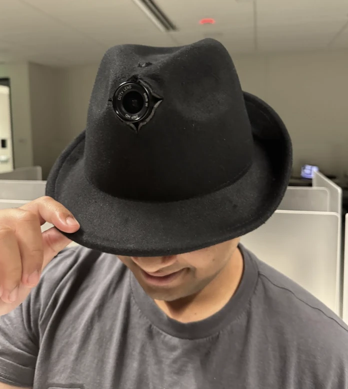 The hat: a black fedora with a camera lens set into the front of its crown, on a crew member tipping its brim.
