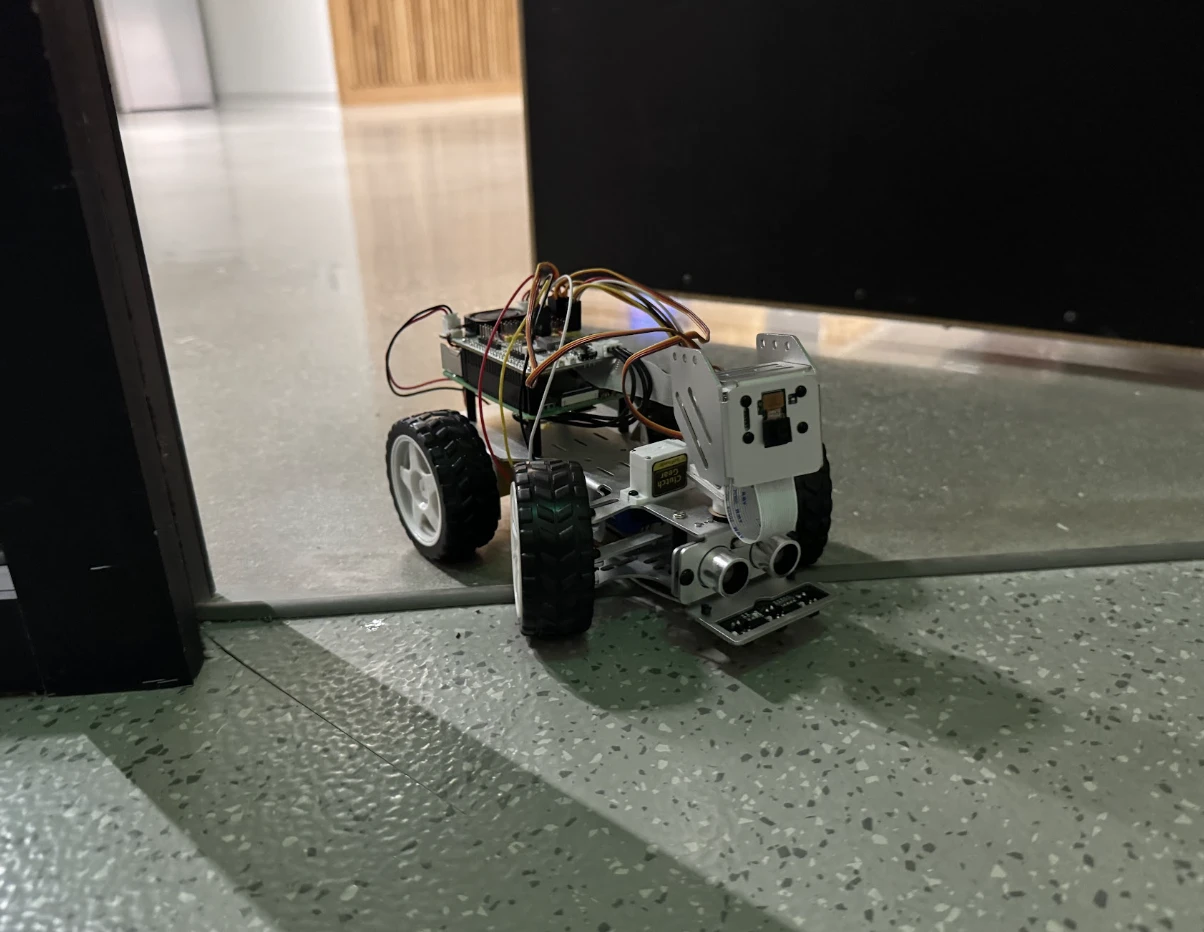 The rover: a small four-wheeled robot car on the floor at a doorway, a camera and a pair of range sensors at its front, wires looped over its boards.